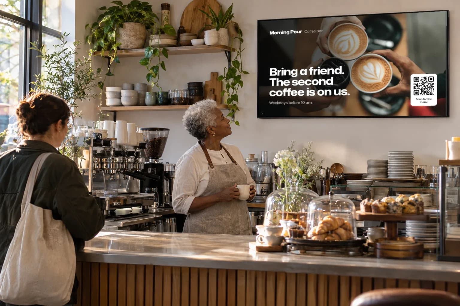 A café owner looks up at her own coffee promotion on the Glowbiz Display in her café